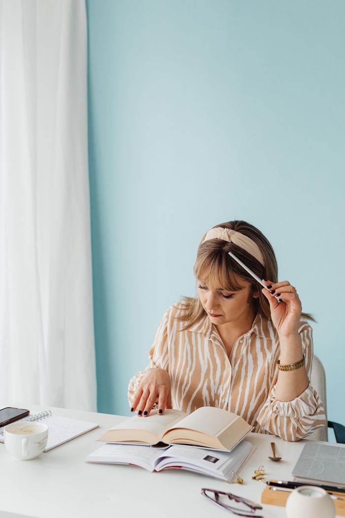Woman in casual attire sitting at a desk, studying with books, in a calm and bright indoor setting.