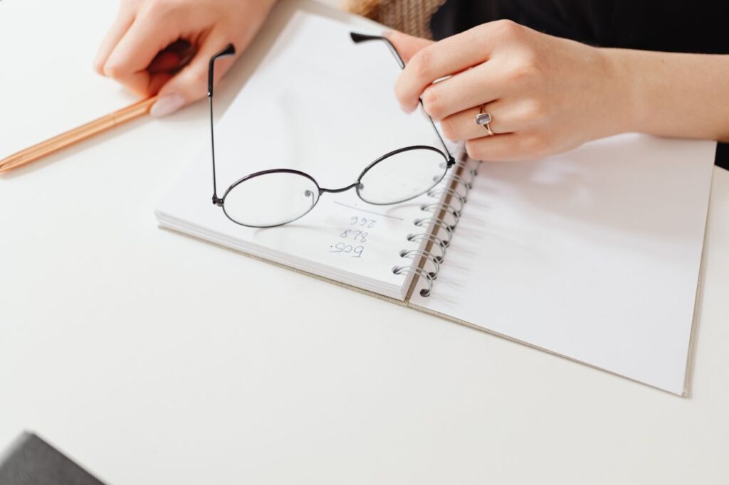 Close-up of a woman writing in a notebook with glasses on the page. Creative workspace concept.
