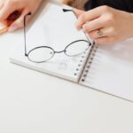 Close-up of a woman writing in a notebook with glasses on the page. Creative workspace concept.